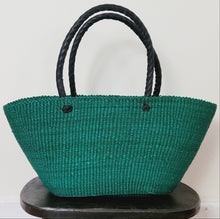 Load image into Gallery viewer, A woven green tote bag with black rope handles, displayed on a dark wooden stool against a plain white wall.
